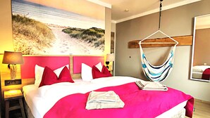 Een hotelkamer met een groot bed, een hangmat, een schilderij met uitzicht op het strand en een lamp.