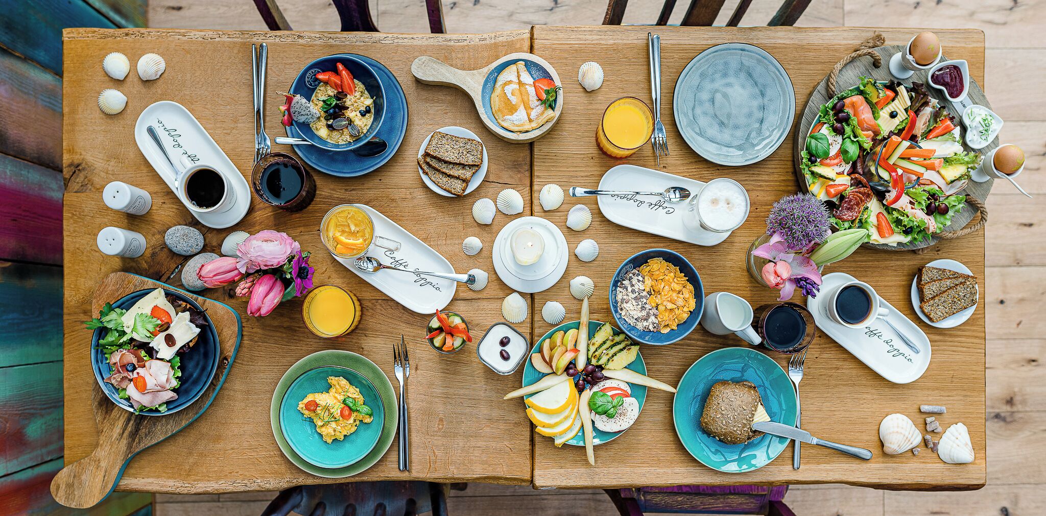 A wooden table with various breakfast items including eggs, toast, cereal, and a salad.