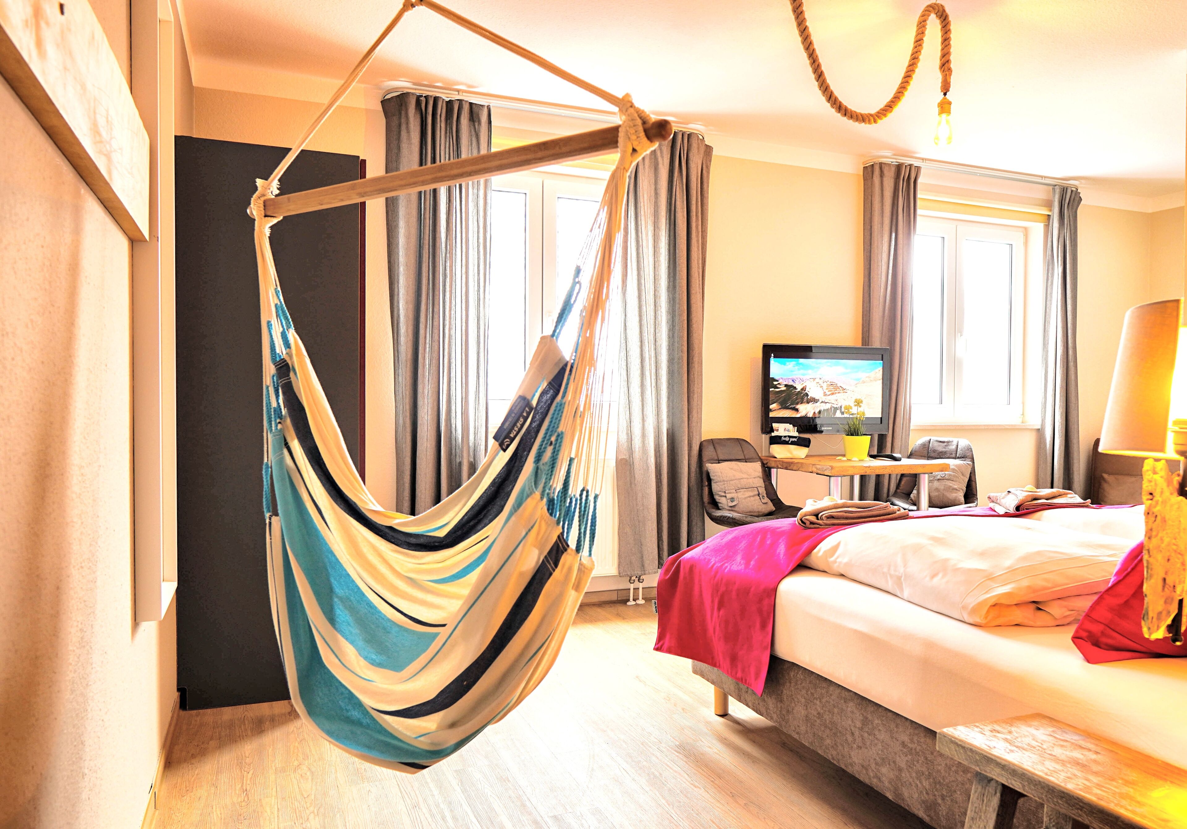 Una habitación de hotel con una cama, una silla colgante, un televisor y un escritorio con lámpara.