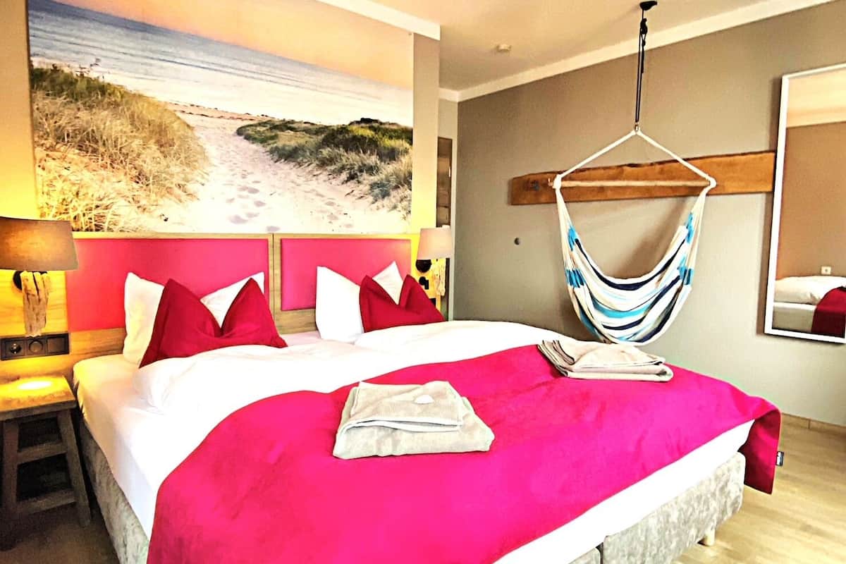 Een hotelkamer met een groot bed, een wanddecoratie met een strandthema, een hangmat en een spiegel.