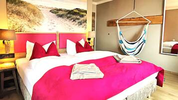 Une chambre d’hôtel avec un grand lit, une fresque murale sur le thème de la plage, un hamac et un miroir.