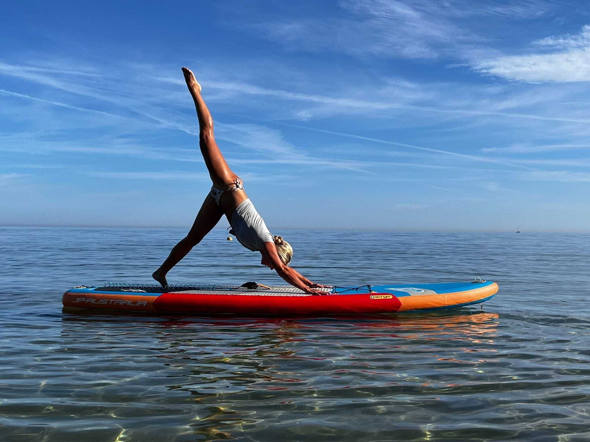 A person performing a yoga pose on a paddleboard in calm waters.