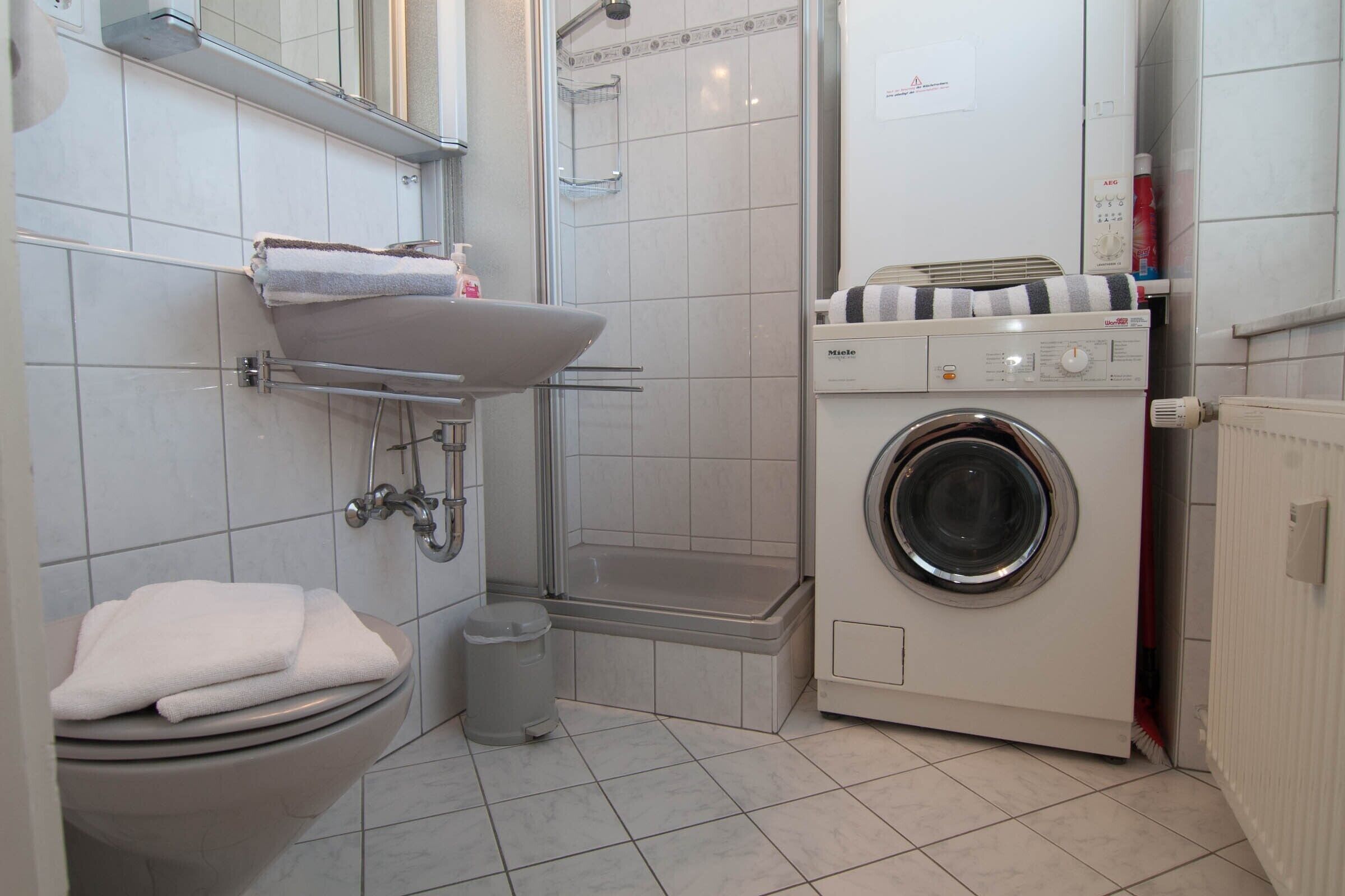 A bathroom with a toilet, sink, shower, and washing machine.