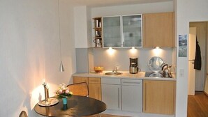 Uma cozinha compacta com área de refeições, apresentando uma mesa redonda, cadeiras, cafeteira e armários.