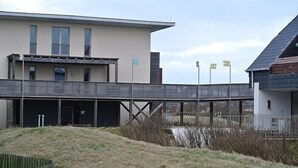 Um edifício moderno com telhado plano, galeria coberta e área gramada na frente.