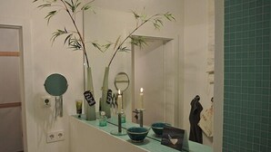 Casa de banho com espelho, dois vasos com plantas, espelho redondo, vela e porta-toalhas.