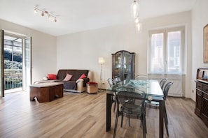 Een ruime woonkamer met een glazen eettafel, een bank, een kast en een groot raam.