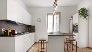 A modern kitchen with white cabinets, a central island with stools, a built-in oven, and a clock on the wall. - Apartment 'Casa Federico ' with Balcony and Wi-Fi (Sestri Levante)