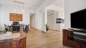 A modern living room with a wooden floor, a dining area with chairs and a table, a TV on a wooden stand, and a hallway leading to a kitchen. - Apartment 'Casa Federico ' with Balcony and Wi-Fi (Sestri Levante)