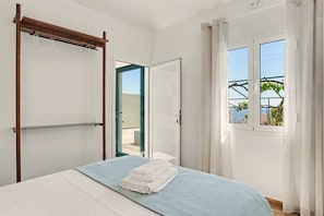 Une chambre avec un lit, un étendoir en bois, une fenêtre avec des rideaux et une vue sur la verdure.