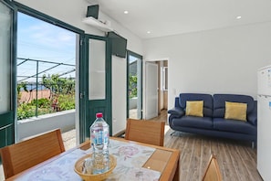 Una sala de estar moderna con un sofá, una mesa de comedor con sillas y un ventanal con vistas a la vegetación.