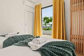 A hotel room with two beds, a view of greenery outside, and a wooden slat door.