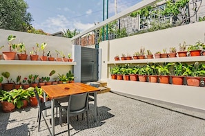 Un patio con una mesa y sillas de madera, rodeado de plantas en macetas sobre estantes.