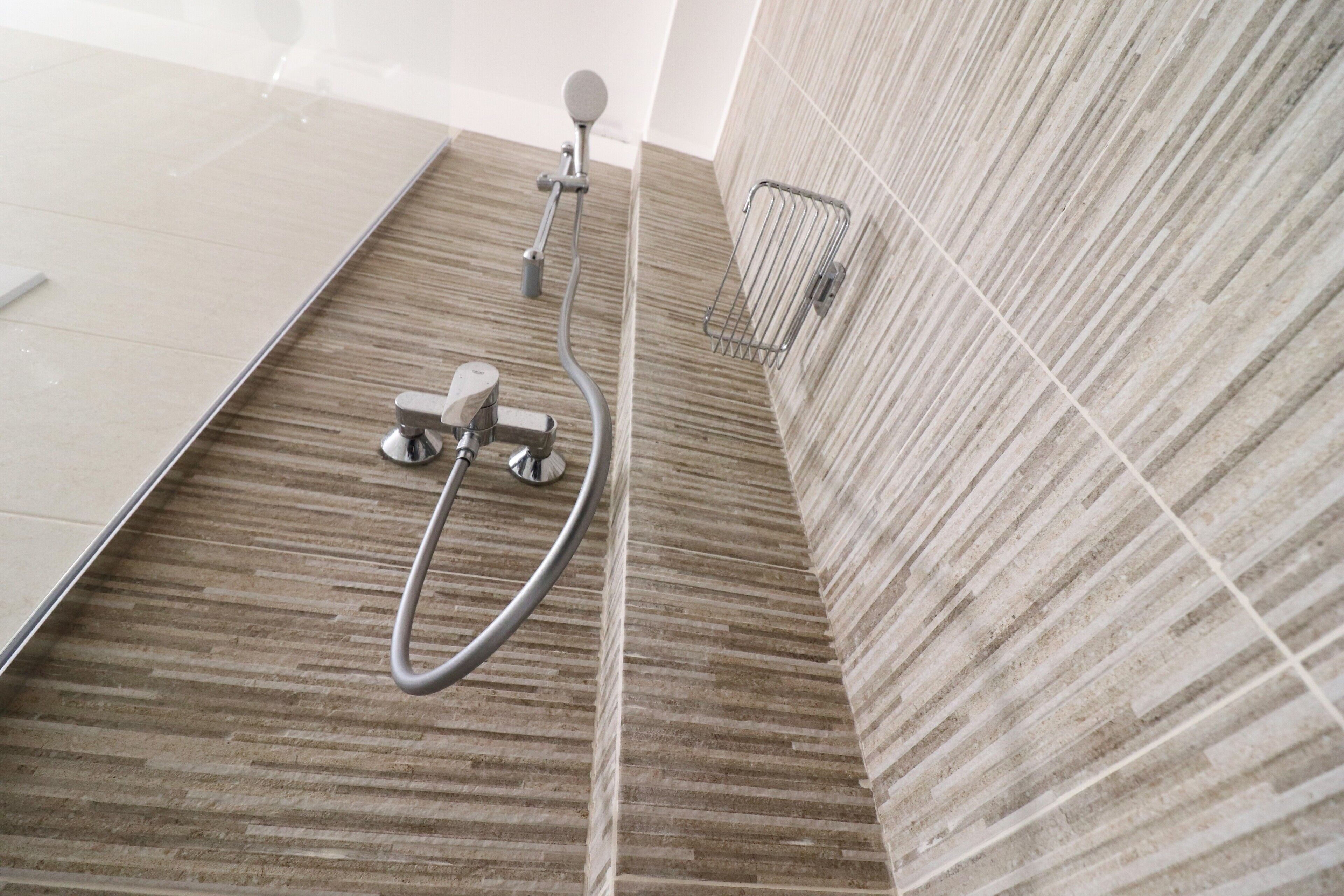 A shower area with a wooden floor, a handheld showerhead, and a wall-mounted hand dryer.