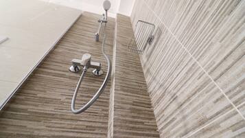 A shower area with a wooden floor, a handheld showerhead, and a wall-mounted hand dryer.