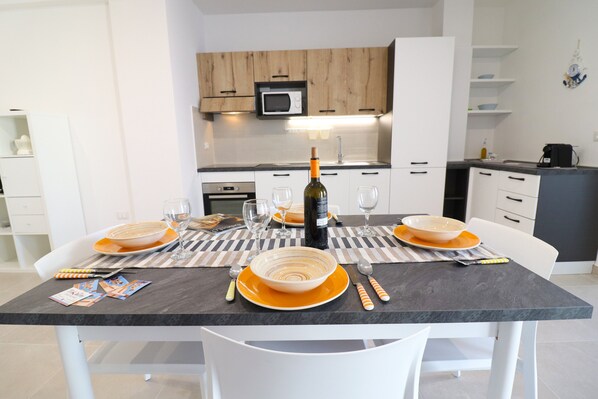 A modern kitchen with white cabinets, a microwave, and a dining table set with orange plates and cutlery.