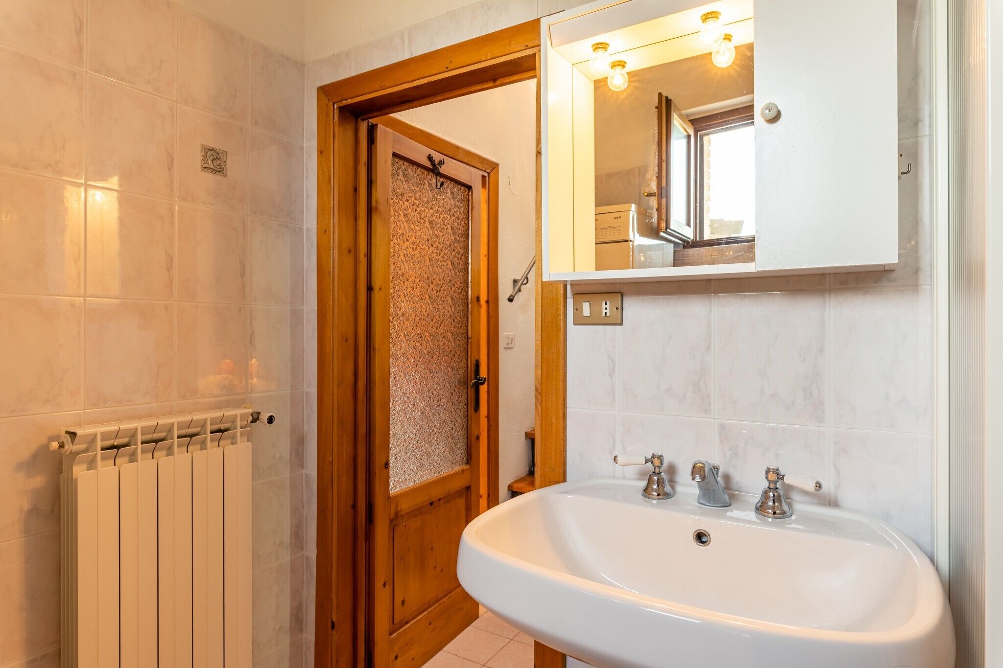 Een badkamer met een witte wastafel, een spiegel en een radiator.