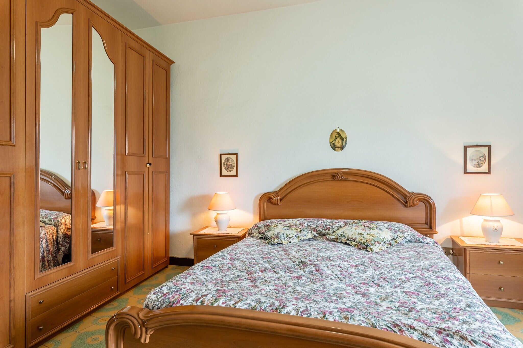 Une chambre à coucher avec un lit en bois, deux tables de chevet avec des lampes, une armoire et un tableau accroché au mur.