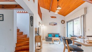 Ein modernes Interieur mit einer Holztreppe, einem Essbereich mit Tisch und Stühlen, einer Couch und einem großen Fenster.