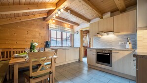A wooden interior with a dining table, chairs, a kitchen with cabinets, a stove, and a window with curtains. - Apartment "Ferienhaus Pichlerhof" with Mountain View, Shared Garden & Wi-Fi (Fundres)