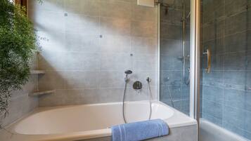 A bathroom with a bathtub, shower, and glass door.