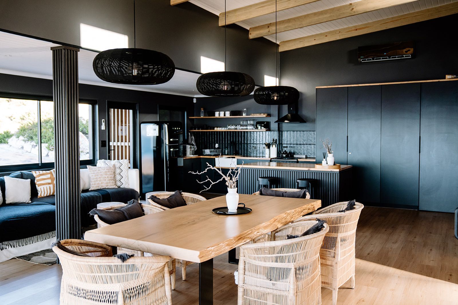 Una cocina moderna con una isla central, electrodomésticos negros y una zona de comedor con sillas de mimbre y una mesa de madera.
