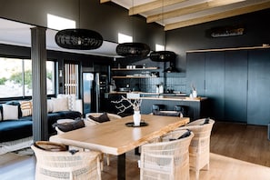 A modern kitchen with a central island, black appliances, and a dining area with wicker chairs and a wooden table.
