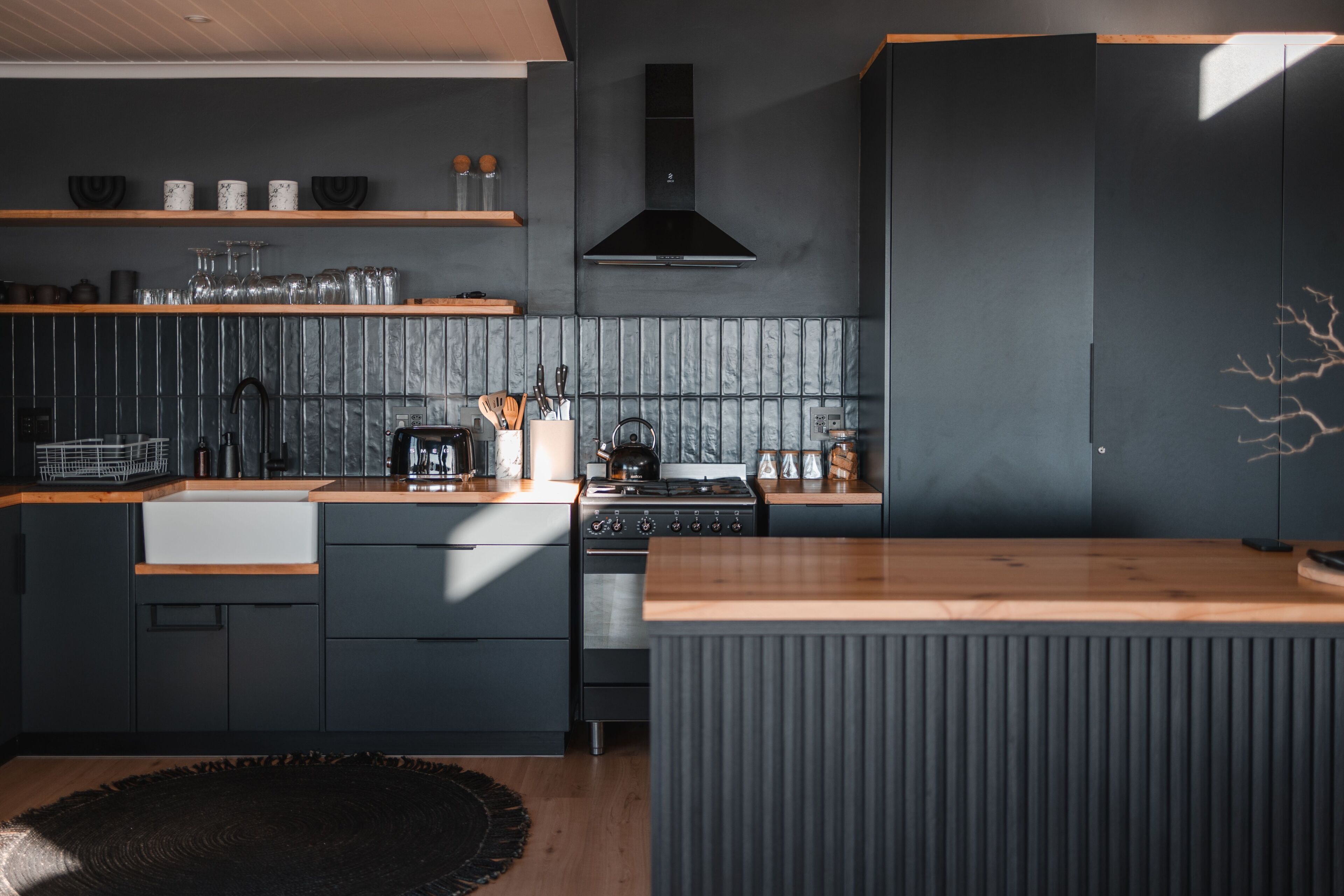 Une cuisine moderne avec des meubles de rangement aux couleurs sombres, un plan de travail en bois et une cuisinière intégrée.