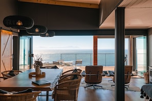 A spacious dining area with a view of the sea, featuring wicker furniture and a wooden table.
