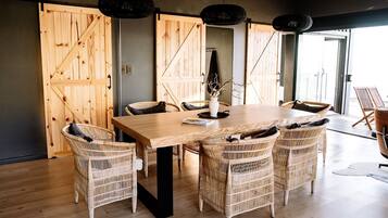 A dining area with a wooden table and wicker chairs, large wooden doors, and pendant lights.