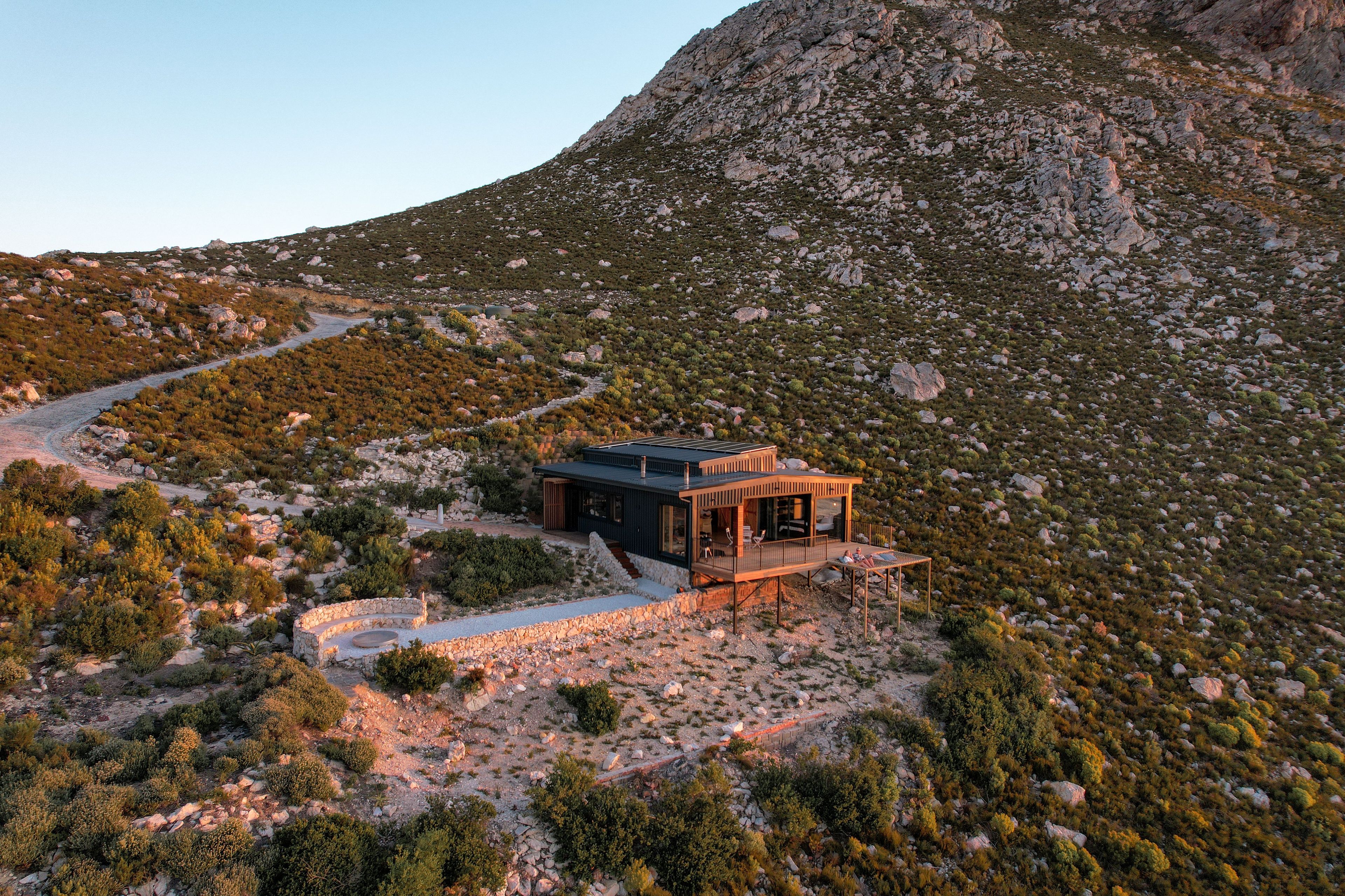 A modern house with a deck, surrounded by rocky terrain and sparse vegetation.