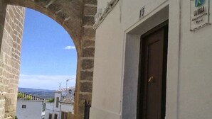 A narrow street with a stone archway leading to a building with a sign reading "LA VILLA Alojamiento Rural".
