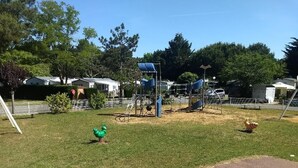Un terrain de jeux avec des toboggans et des structures d’escalade, entouré d’herbe et d’arbres.