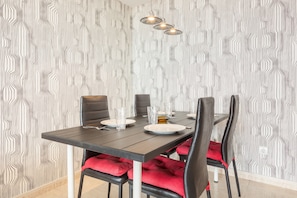 Un comedor con una mesa dispuesta para cuatro, sillas con cojines rojos y un papel tapiz estampado.