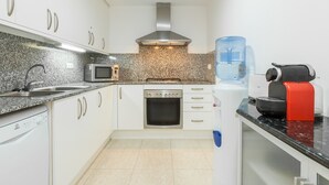 Eine moderne Küche mit weißen Schränken, einer Edelstahl-Dunstabzugshaube, einer Mikrowelle, einem Backofen, einem Wasserspender und einer Kaffeemaschine.