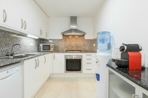 A modern kitchen with white cabinets, a stainless steel range hood, a microwave, a built-in oven, a water dispenser, and a coffee maker.