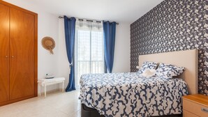 Ein Schlafzimmer mit einem Bett, einem Holzschrank, einem kleinen weißen Tisch und einem Fenster mit blauen Vorhängen.