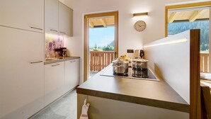 A modern kitchen with white cabinets, a wooden ceiling, a large window, and a clock on the wall.