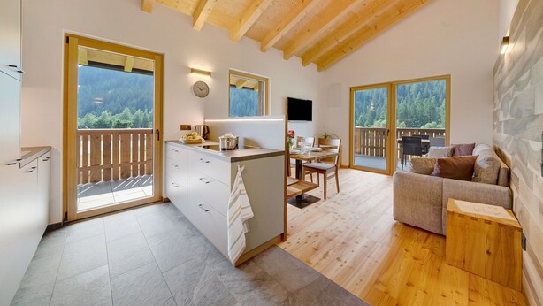 A modern kitchen with a wooden ceiling, a dining area with a table and chairs, and a living space with a sofa and a TV.