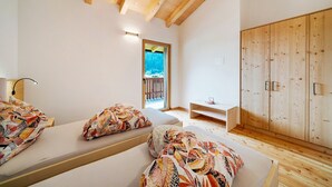 A room with wooden beams, a bed with patterned bedding, a wooden wardrobe, and a view through a window.