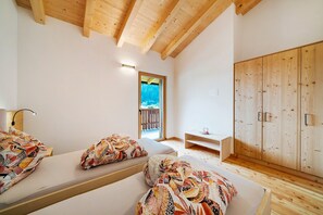 Una habitación con vigas de madera, una cama con ropa de cama estampada, un armario de madera y vistas a través de una ventana.