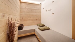 Een kleine, gezellige kamer met een houten schuine plafond, een bank met kussens, en een muur met de tekst 'Relax' en decoratieve bloemen.