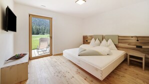 Een slaapkamer met een bed, een televisie, een houten hoofdbord, een klein nachtkastje en uitzicht op een grasveld door een glazen deur.