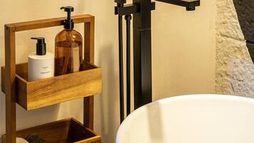 A bathroom with a white bathtub, wooden shelves with toiletries, and rose petals on the tub.