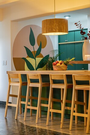 A dining area with a wooden table, six chairs, a hanging light fixture, and a wall with a large abstract painting.