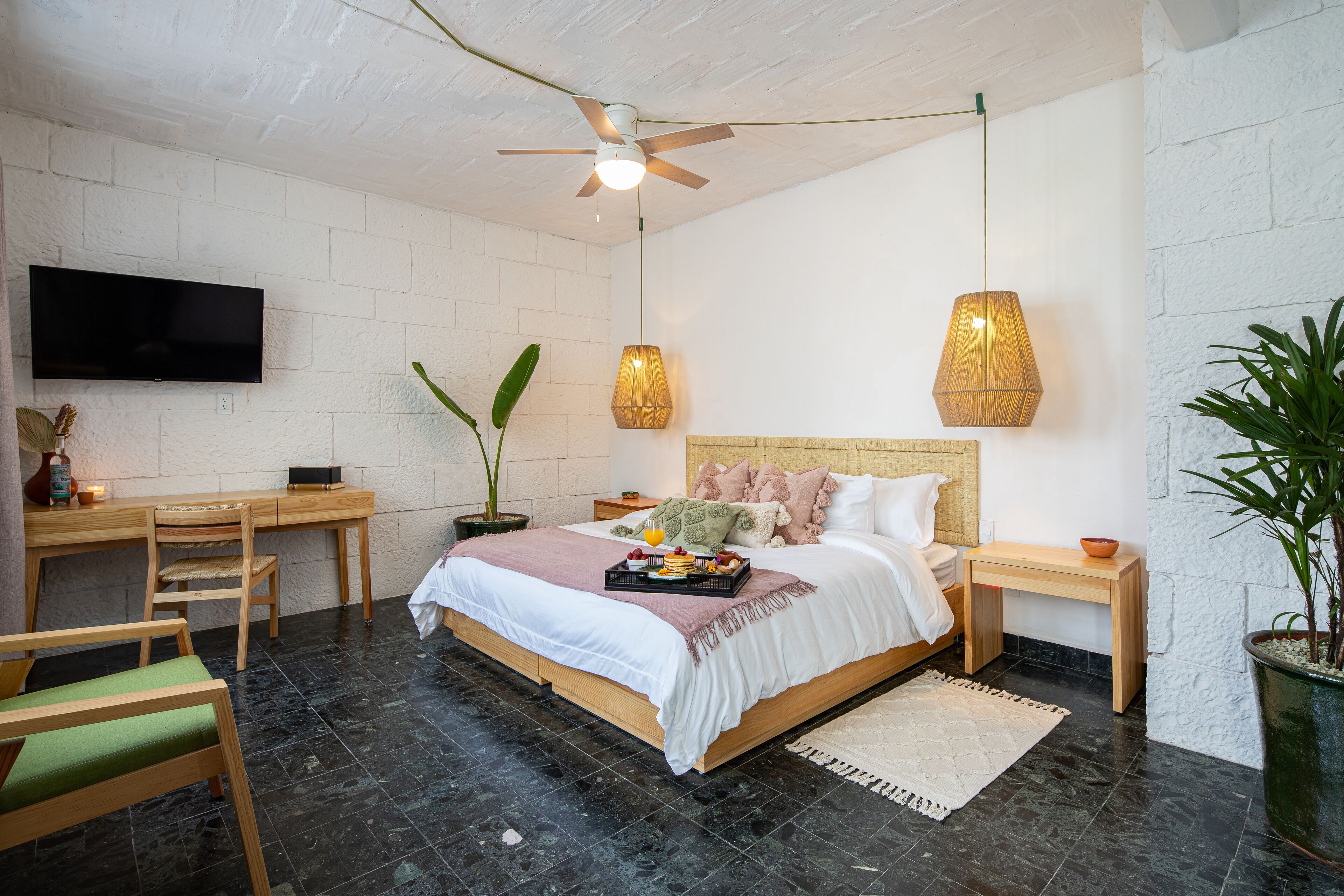 A bedroom with a bed, bedside tables, a desk, a chair, a TV, and a ceiling fan.