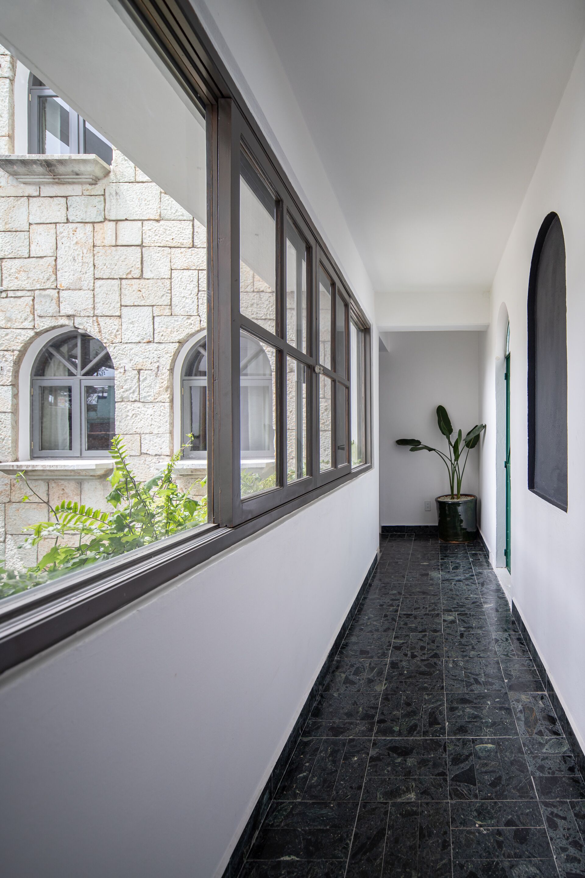 Un pasillo con ventanas amplias, una planta en maceta y un edificio de piedra a la vista.