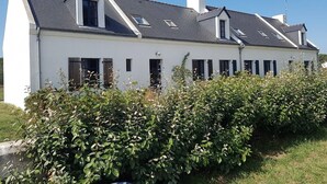 Ein weißes, zweistöckiges Haus mit grauem Dach, zahlreichen Fenstern und einem Schornstein.