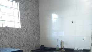 Una cocina con una mesa de comedor y sillas, armarios blancos, encimera negra y una ventana con persianas.