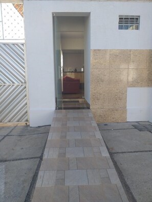 Un sendero lleva a una habitación con sofá rojo, piso de baldosas y una cocina parcialmente visible.